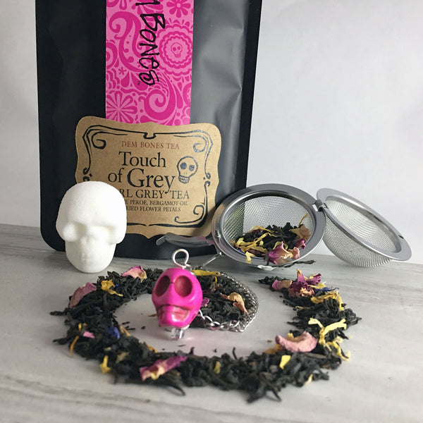 Black and Pink Tea Packaging, Ear grey tea in a swirl on light background, one skull shaped sugar cube, pink skull bead with Tea Infuser Ball