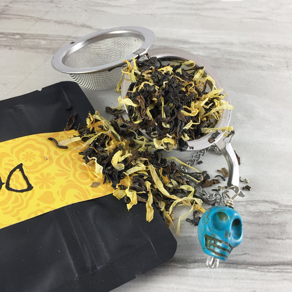 Black bag with yellow graphics band, Marigold tea spilling out of tea ball with blue skull bead,
