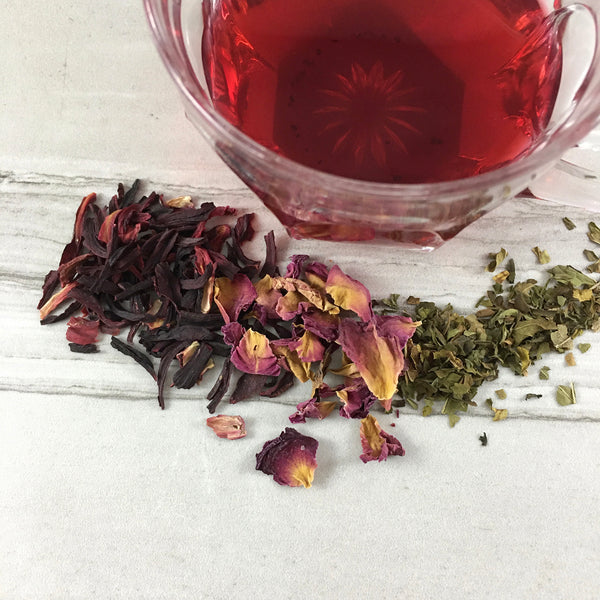 Tea spread on white tile, Red tea in vintage glass cup,  Dried Hibiscus Rose Petals and  Mint