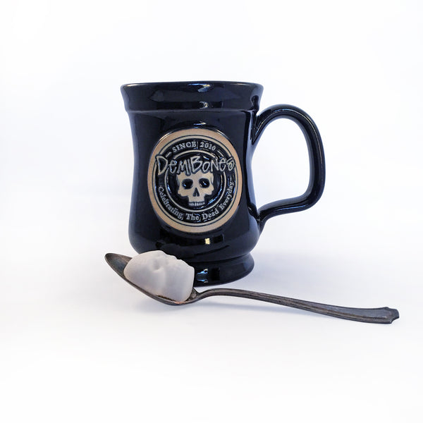Skull Sugar Cube Balanced on a silver spoon, Black Coffee Mug behind, Large circular Dem Bones Since 2010 Logo