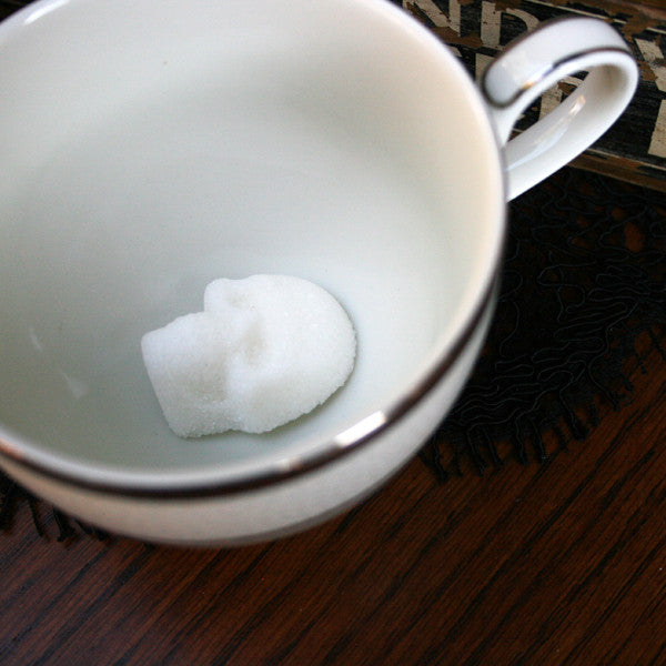 Skull Sugar Cube in bottom of White Tea Cup with Silver rim. On dark wood background